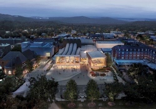 An aerial view of a modern building complex with illuminated areas, surrounded by greenery and other structures at dusk.