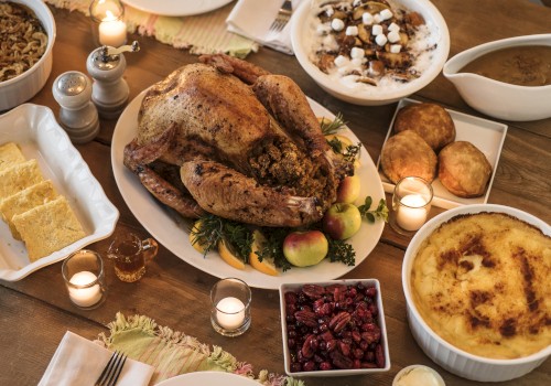 A Thanksgiving meal featuring a roast turkey, stuffing, cranberries, mashed potatoes, and pies, arranged with candles on a table.