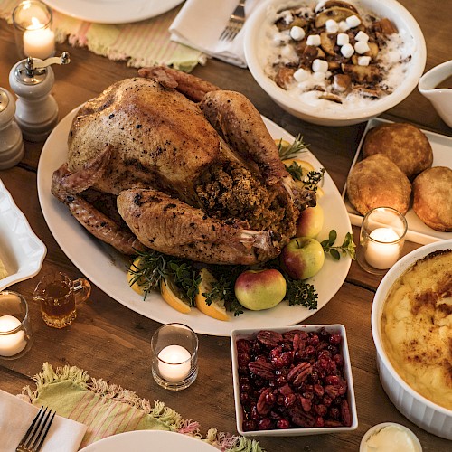 A Thanksgiving meal featuring a roast turkey, stuffing, cranberries, mashed potatoes, and pies, arranged with candles on a table.