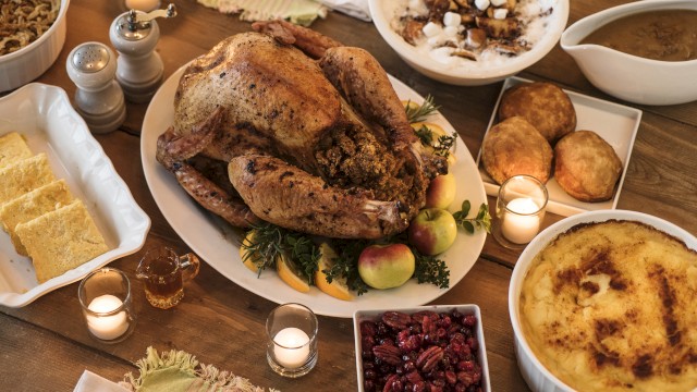 A Thanksgiving meal featuring a roast turkey, stuffing, cranberries, mashed potatoes, and pies, arranged with candles on a table.