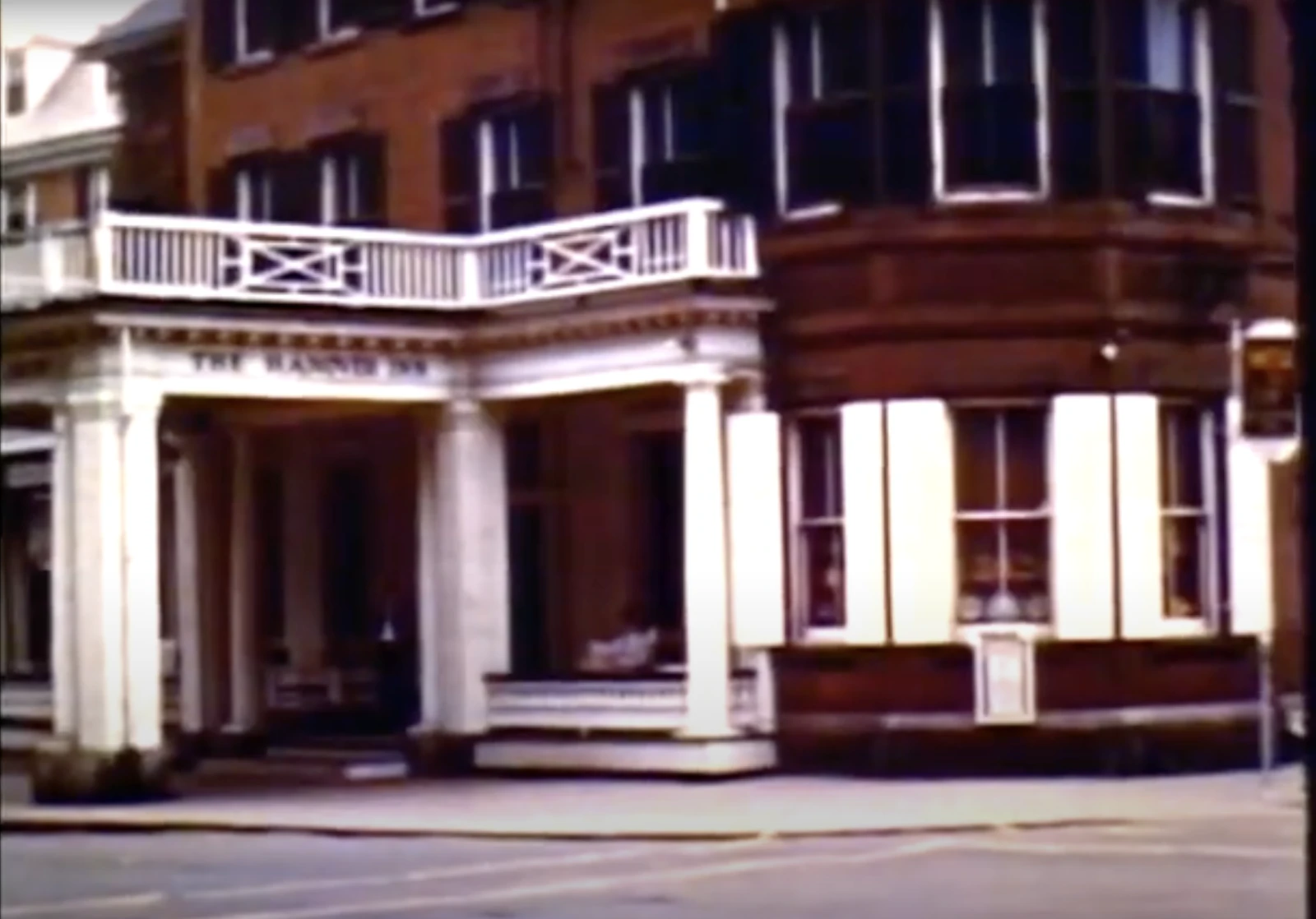 The image shows a historic building with white columns and a brick facade, likely a hotel or similar establishment on a street corner.