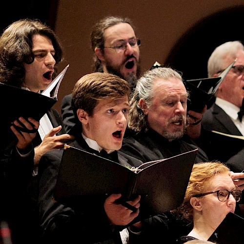 A choir of diverse individuals passionately sings from sheet music during a performance.