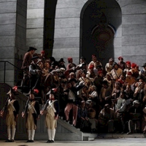 A staged scene with people in historical costumes on stairs, possibly from a theater or opera performance.