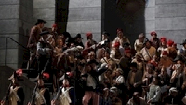 A staged scene with people in historical costumes on stairs, possibly from a theater or opera performance.