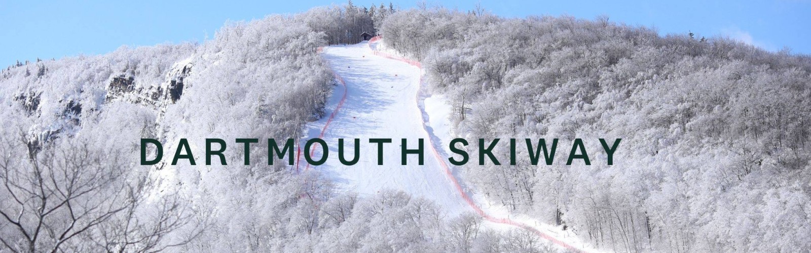 A snowy ski slope winds up a frosted hill at Dartmouth Skiway, with bare trees dusted in white and a clear blue sky.