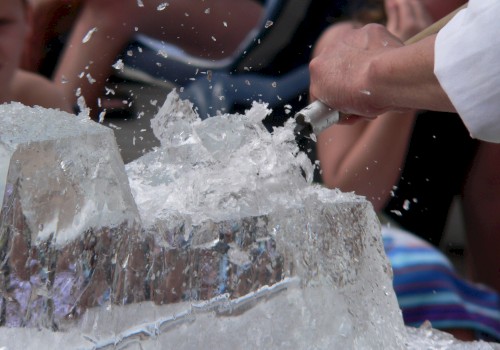 Ice blocks being hacked or chipped with a knife, splashing shards in mid-air, while onlookers watch closely.
