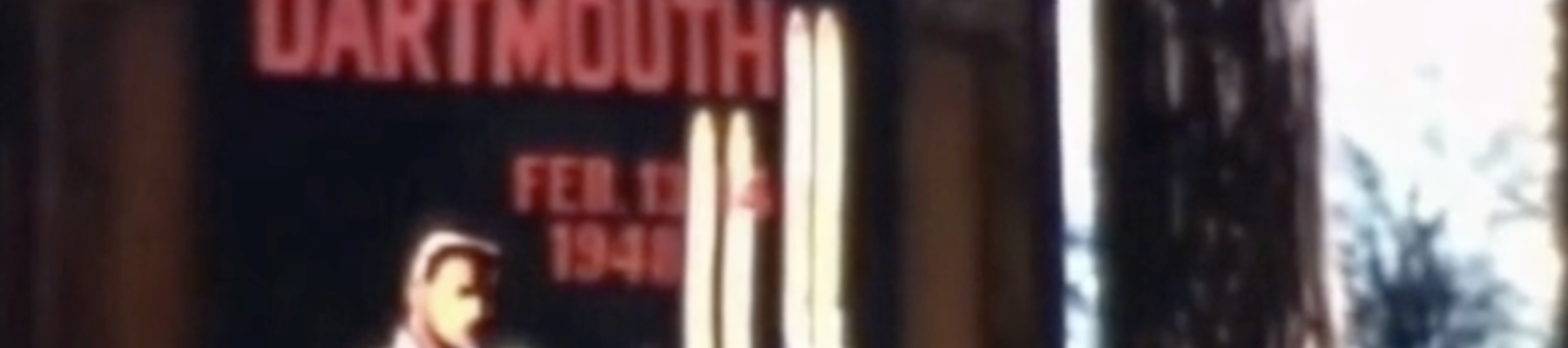 A blurry sign reading “DARTMOUTH” in red letters, with a person portrait and some tall white shapes (possibly sails or lights) beside it.
