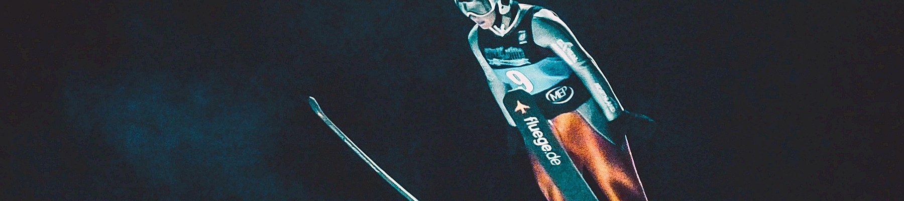 A person dressed in ski gear and a helmet is skiing or free-falling in a dark environment.