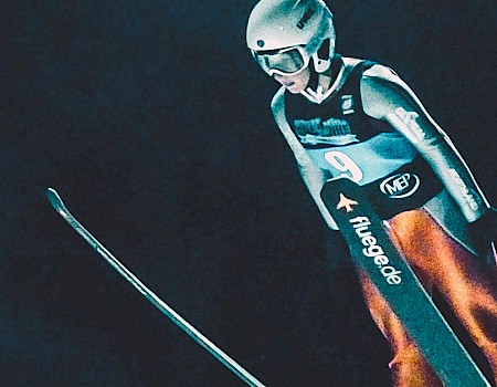 A person dressed in ski gear and a helmet is skiing or free-falling in a dark environment.