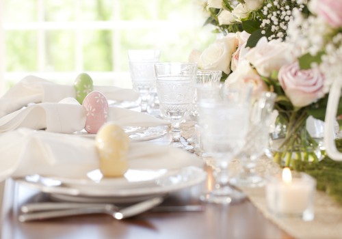 A beautifully set Easter table with pastel eggs, floral arrangements, wine glasses, and a candle in natural light.