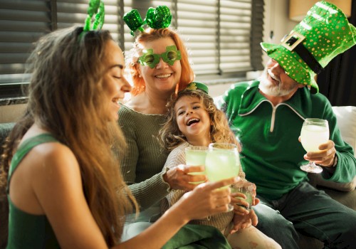 A family celebrates St. Patrick's Day with green accessories, laughing, and enjoying drinks inside a cozy home.