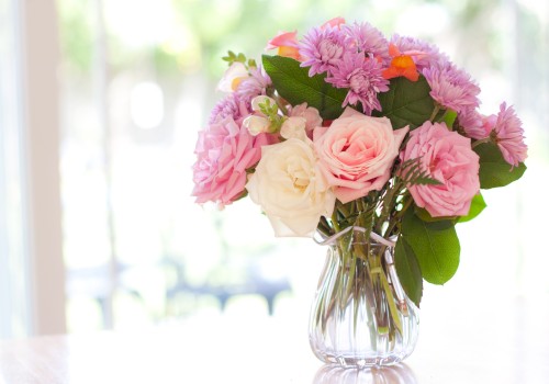 A clear vase holds a bouquet of pink and white flowers, including roses and chrysanthemums, set against a softly blurred background.