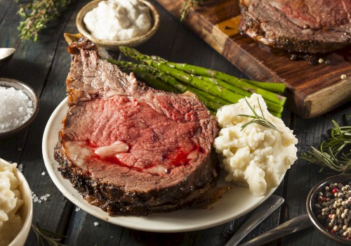 A roasted ribeye steak with mashed potatoes, green asparagus, and various seasonings on a dark wooden table.
