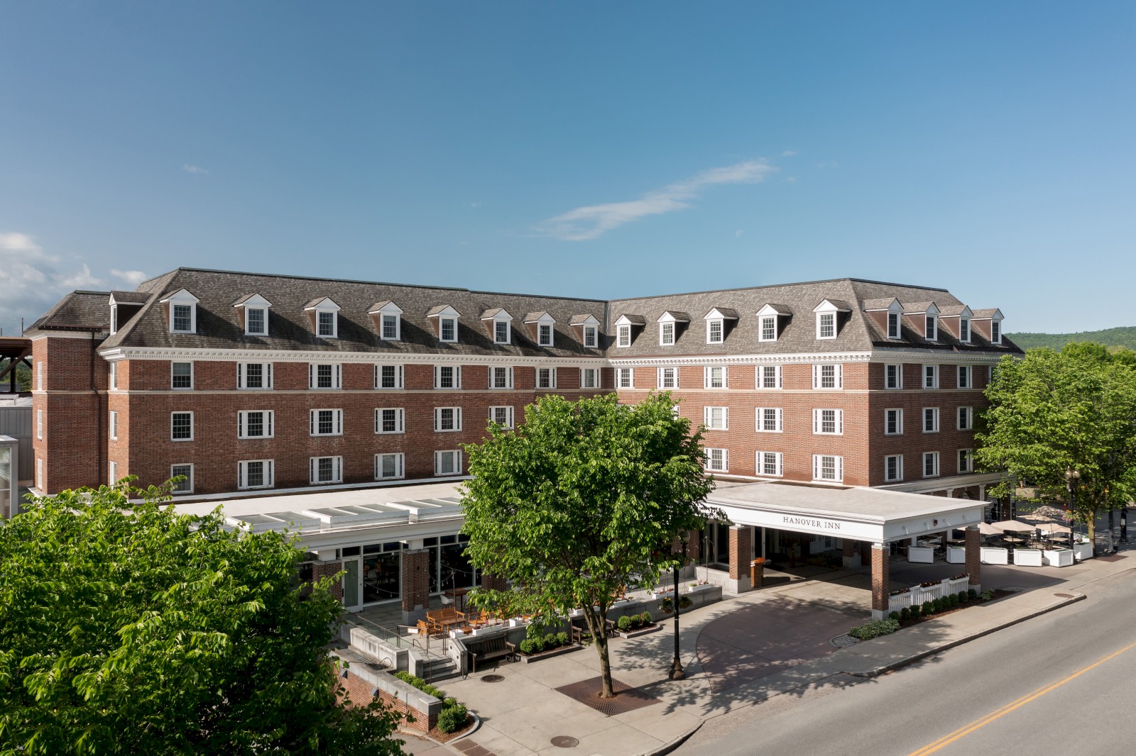 This image shows the Hanover Inn, a historic brick hotel with a covered entrance and outdoor seating, under a clear blue sky.