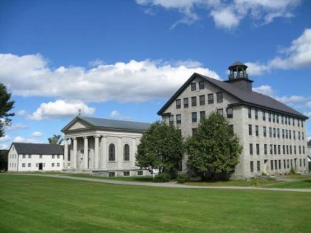 The image shows a large historic building with classical and modern architectural elements, surrounded by green grass and a blue sky with clouds.
