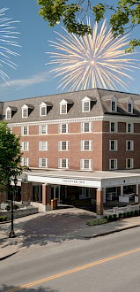 Celebrating with colorful fireworks over the Hanover Inn, a charming brick hotel, on a bright, partly cloudy day.