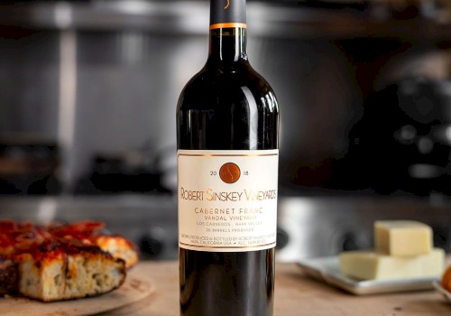 A bottle of Robert Sinskey Vineyards Cabernet Franc wine stands on a kitchen counter with pizza and cheese in the background.