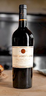 A bottle of Robert Sinskey Vineyards Cabernet Franc wine from Napa Valley, surrounded by pizza and cheese on a kitchen counter.