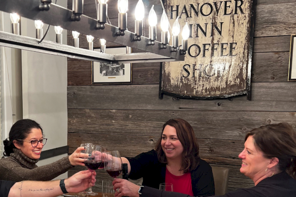 People are happily toasting with glasses of red wine at a dinner table in a rustic restaurant.