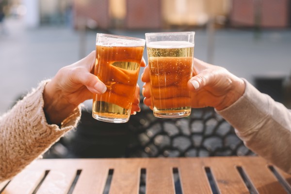 Two people are clinking glasses of beer outdoors during daylight.